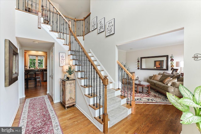 stairs featuring a towering ceiling, wood-type flooring, and crown molding