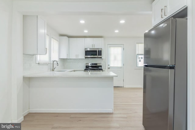 kitchen featuring light hardwood / wood-style floors, white cabinets, kitchen peninsula, sink, and appliances with stainless steel finishes