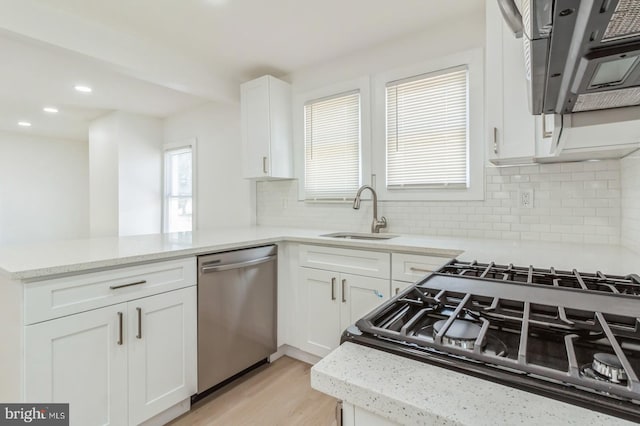 kitchen with white cabinets, stainless steel dishwasher, sink, and light wood-type flooring