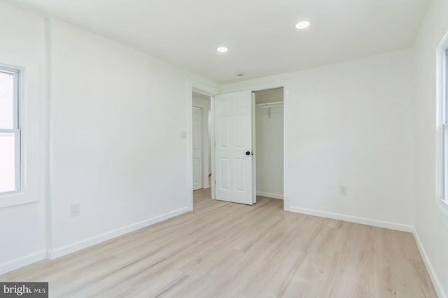 unfurnished bedroom featuring light hardwood / wood-style floors, multiple windows, and a closet