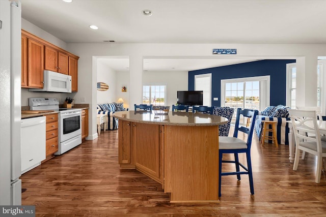 kitchen featuring white appliances, dark hardwood / wood-style floors, a breakfast bar area, and a center island