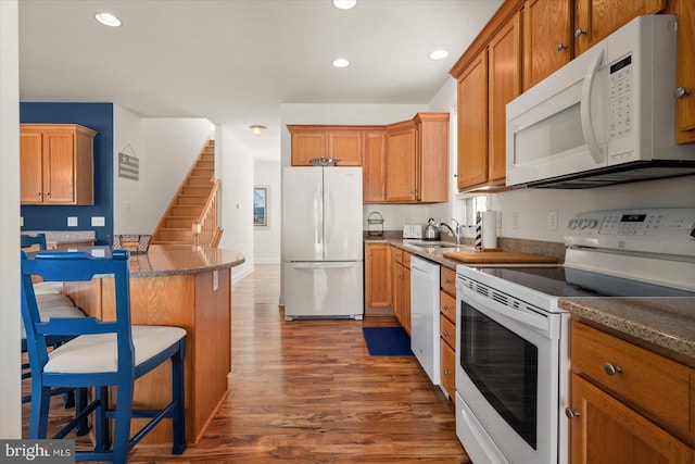 kitchen featuring a kitchen breakfast bar, dark wood-type flooring, dark stone counters, and white appliances