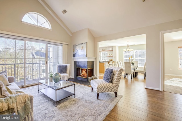 living room featuring a multi sided fireplace, wood-type flooring, a chandelier, and high vaulted ceiling