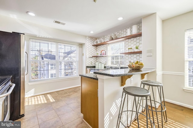 kitchen with stainless steel appliances, a kitchen bar, a healthy amount of sunlight, and backsplash