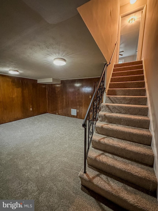 stairs with wood walls, a textured ceiling, and carpet floors