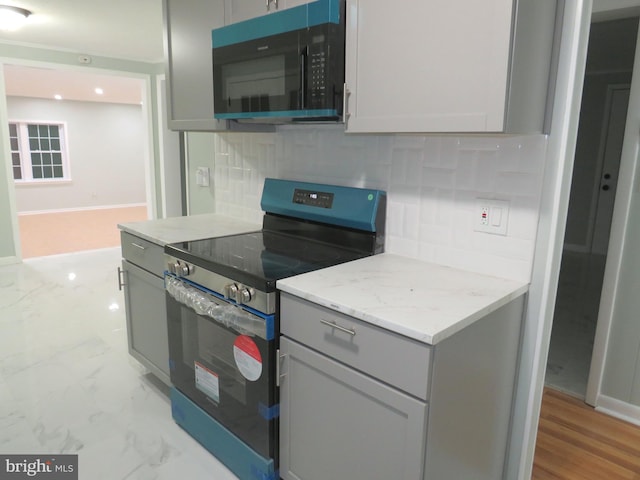 kitchen featuring light stone countertops, backsplash, gray cabinets, and stainless steel electric range oven