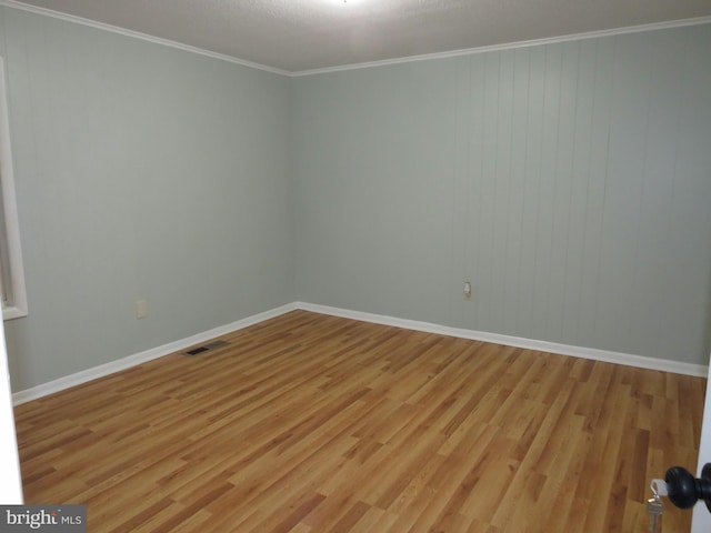 empty room featuring crown molding, wood walls, and light wood-type flooring