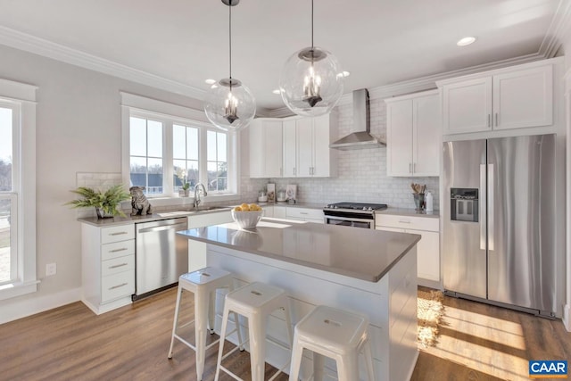 kitchen with wall chimney exhaust hood, a kitchen island, white cabinetry, light wood-type flooring, and appliances with stainless steel finishes