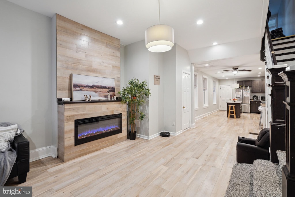 living room with ceiling fan, a tile fireplace, and light hardwood / wood-style flooring