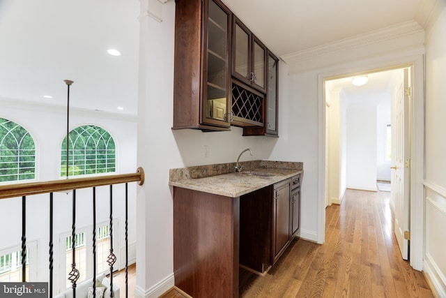 bar featuring dark brown cabinets, light hardwood / wood-style flooring, sink, and light stone counters