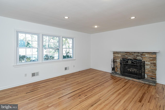 unfurnished living room with plenty of natural light, a stone fireplace, and light hardwood / wood-style flooring