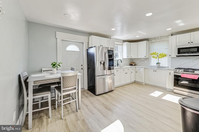 kitchen featuring stainless steel appliances, light hardwood / wood-style floors, sink, backsplash, and white cabinets