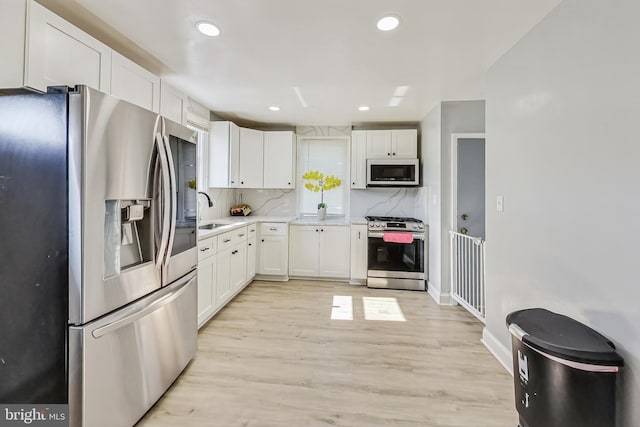 kitchen featuring backsplash, appliances with stainless steel finishes, sink, light hardwood / wood-style floors, and white cabinets