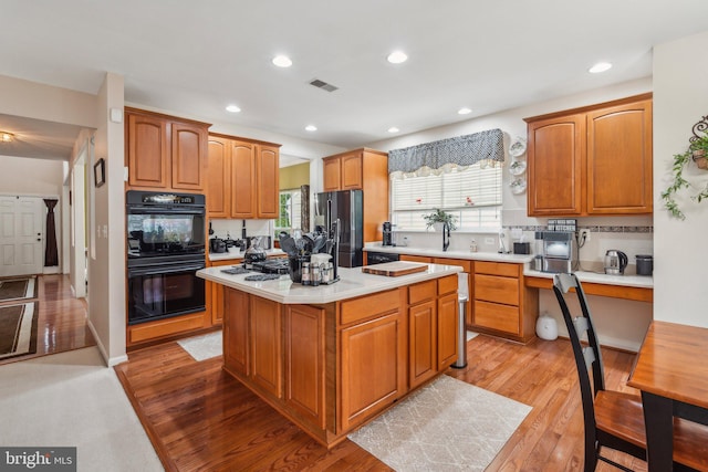 kitchen featuring a center island, stainless steel fridge with ice dispenser, black double oven, light wood-type flooring, and decorative backsplash