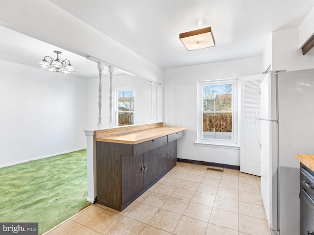 kitchen featuring light carpet, dark brown cabinetry, a notable chandelier, white fridge, and butcher block counters