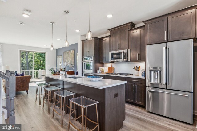 kitchen featuring stainless steel appliances, a kitchen bar, hanging light fixtures, sink, and an island with sink