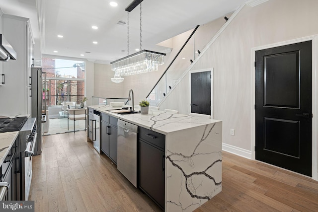 kitchen featuring stainless steel appliances, light wood-type flooring, hanging light fixtures, sink, and a kitchen island with sink