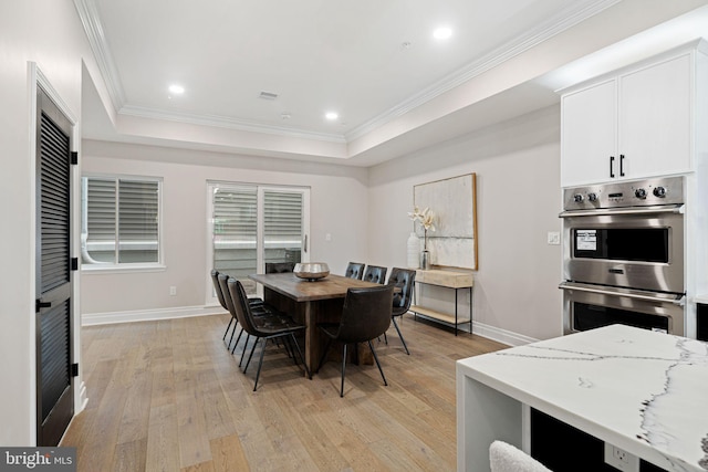 dining room with a tray ceiling, light hardwood / wood-style floors, and crown molding