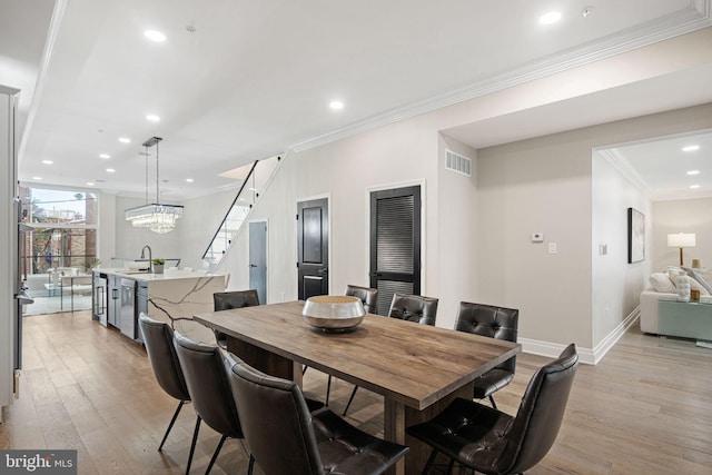 dining area with a notable chandelier, sink, crown molding, light wood-type flooring, and wine cooler