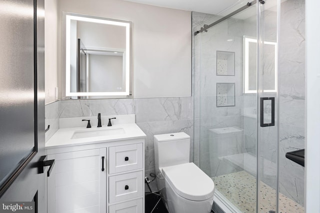 bathroom featuring toilet, vanity, tile walls, and a shower with shower door