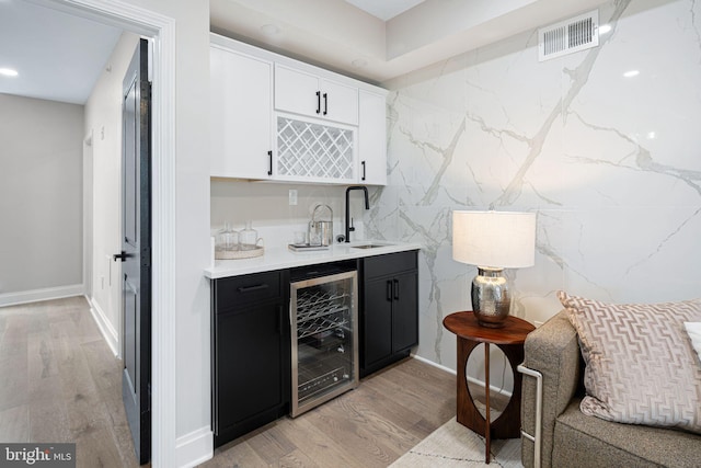 bar with light wood-type flooring, beverage cooler, sink, and white cabinets