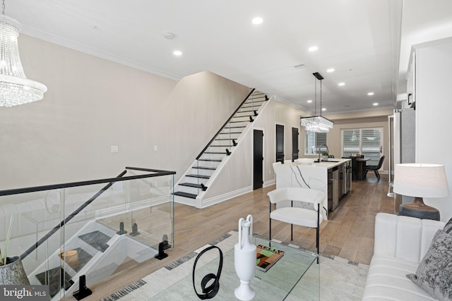 living room featuring ornamental molding, sink, a notable chandelier, and light hardwood / wood-style floors