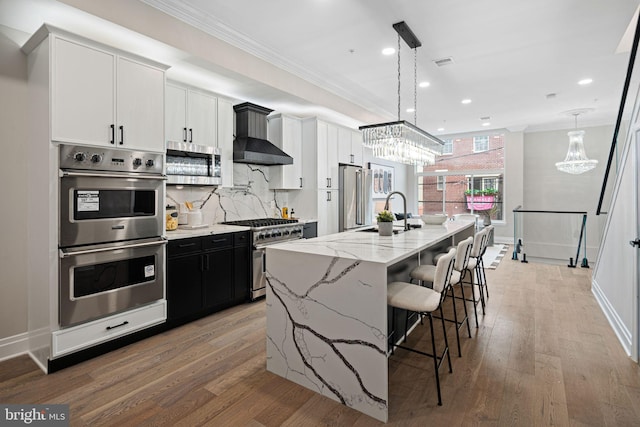 kitchen featuring white cabinets, high end appliances, hanging light fixtures, a large island, and wall chimney range hood