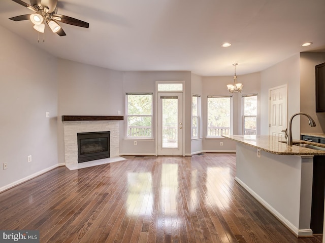 unfurnished living room featuring baseboards, dark wood-style flooring, a fireplace, a sink, and recessed lighting