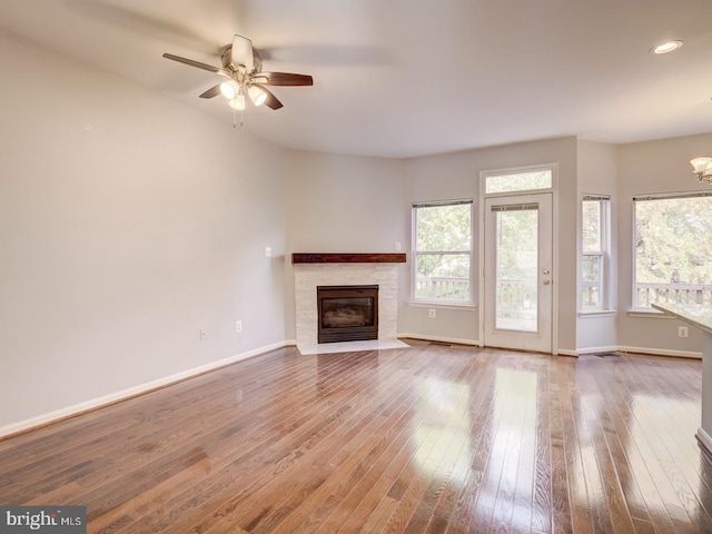 unfurnished living room with hardwood / wood-style flooring, recessed lighting, ceiling fan with notable chandelier, a fireplace with flush hearth, and baseboards