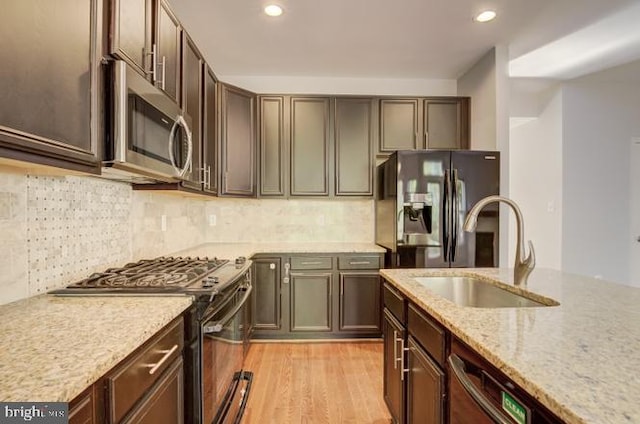 kitchen featuring sink, tasteful backsplash, light stone countertops, light wood-type flooring, and appliances with stainless steel finishes