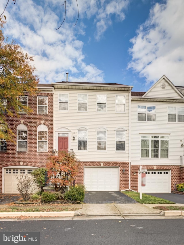 view of property featuring driveway, brick siding, and an attached garage