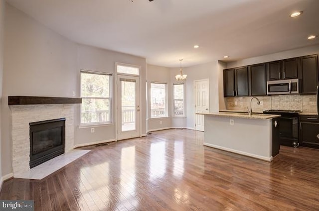 kitchen with black range with electric cooktop, open floor plan, dark wood-style floors, tasteful backsplash, and stainless steel microwave