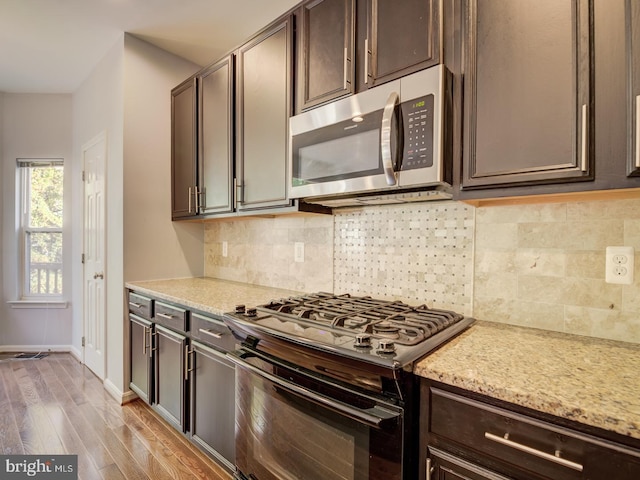 kitchen featuring dark brown cabinetry, decorative backsplash, light wood-style flooring, stainless steel microwave, and gas stove