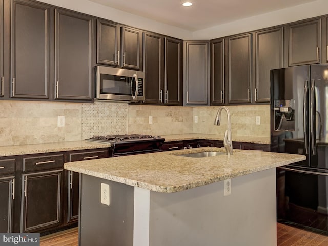 kitchen featuring decorative backsplash, light stone counters, wood finished floors, stainless steel appliances, and a sink