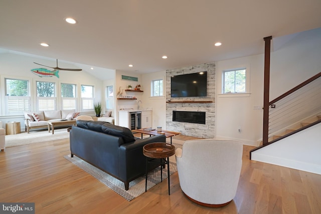 living room featuring light hardwood / wood-style floors, ceiling fan, a fireplace, beverage cooler, and vaulted ceiling