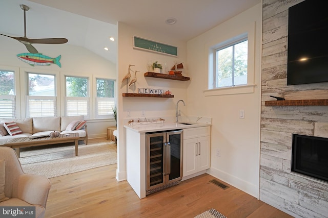 bar with vaulted ceiling, sink, white cabinetry, light hardwood / wood-style flooring, and wine cooler