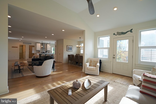 living room featuring ceiling fan with notable chandelier, light wood-type flooring, and vaulted ceiling