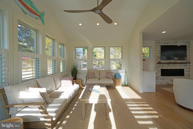 sunroom featuring a stone fireplace, a healthy amount of sunlight, ceiling fan, and vaulted ceiling