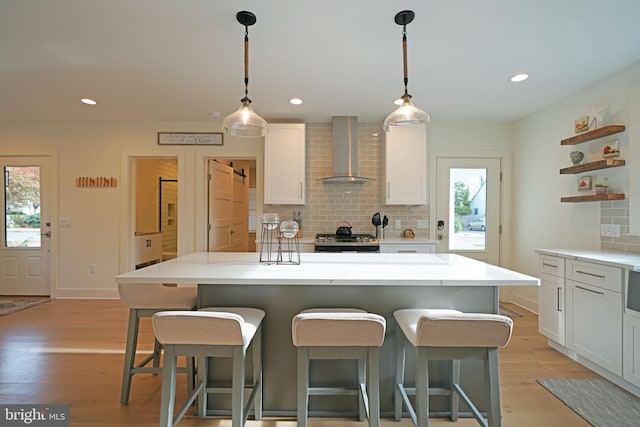 kitchen with a kitchen island, wall chimney range hood, stainless steel range, and plenty of natural light