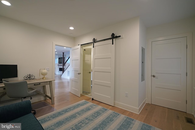 office space featuring light wood-type flooring, electric panel, and a barn door