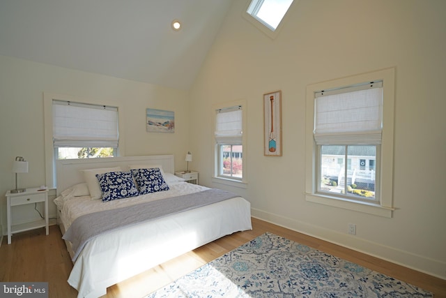 bedroom with high vaulted ceiling, multiple windows, a skylight, and hardwood / wood-style flooring