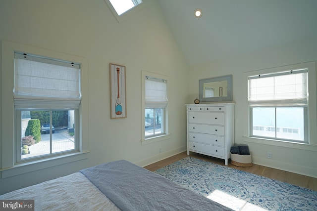 bedroom with high vaulted ceiling, a skylight, and hardwood / wood-style floors