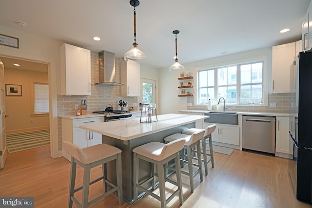 kitchen with appliances with stainless steel finishes, wall chimney exhaust hood, white cabinets, and a center island