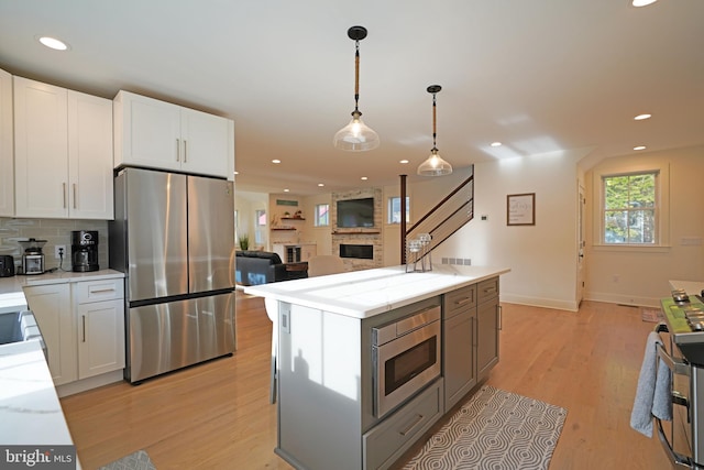 kitchen with white cabinetry, appliances with stainless steel finishes, tasteful backsplash, light wood-type flooring, and pendant lighting