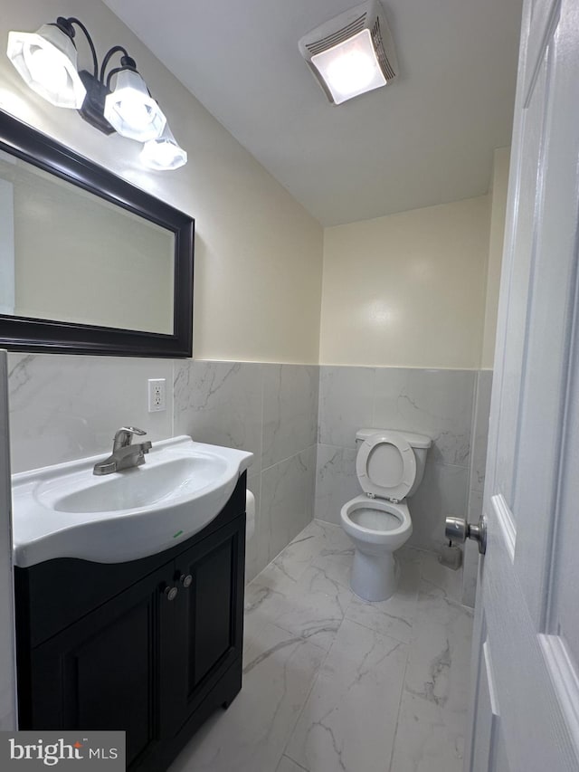 bathroom with toilet, vanity, and tile walls