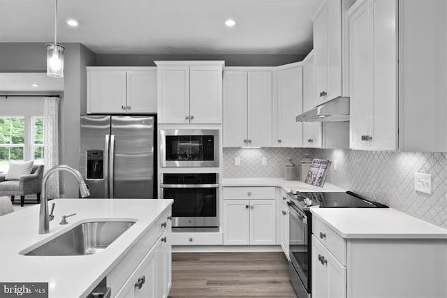 kitchen featuring sink, appliances with stainless steel finishes, decorative light fixtures, wood-type flooring, and white cabinets