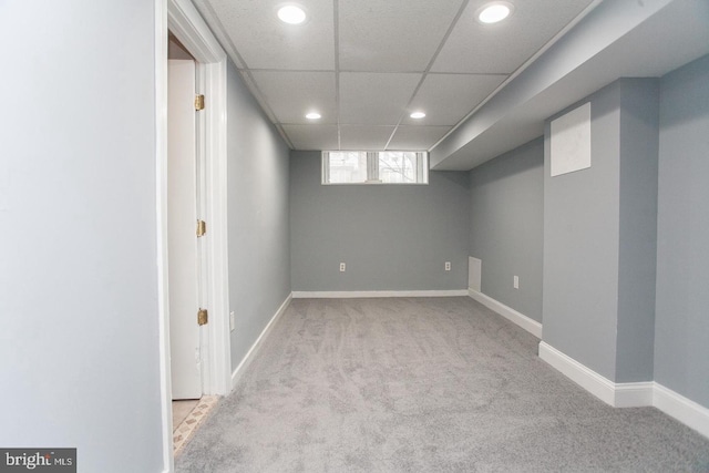 basement with a paneled ceiling and light colored carpet