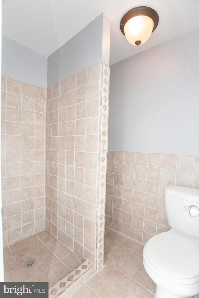 bathroom featuring tile patterned floors, toilet, tiled shower, and tile walls