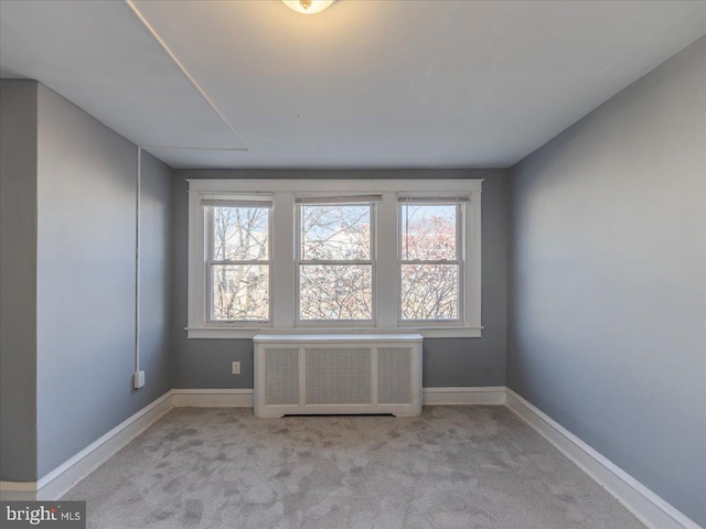 empty room featuring a wealth of natural light, light carpet, and radiator heating unit