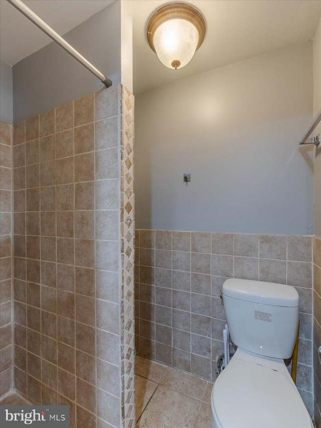 bathroom featuring a shower, tile patterned floors, toilet, and tile walls